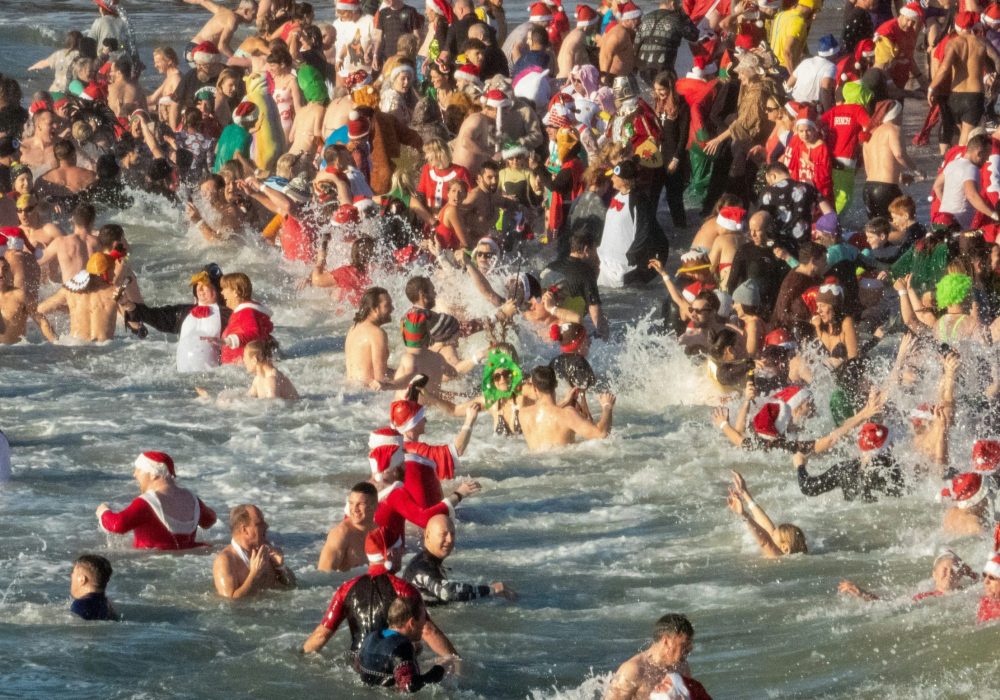 swimmers, some with christmas hats, costumes in the sea.