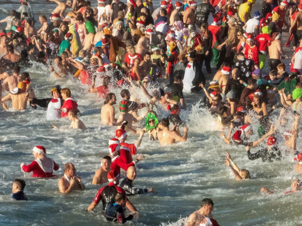 swimmers, some with christmas hats, costumes in the sea.