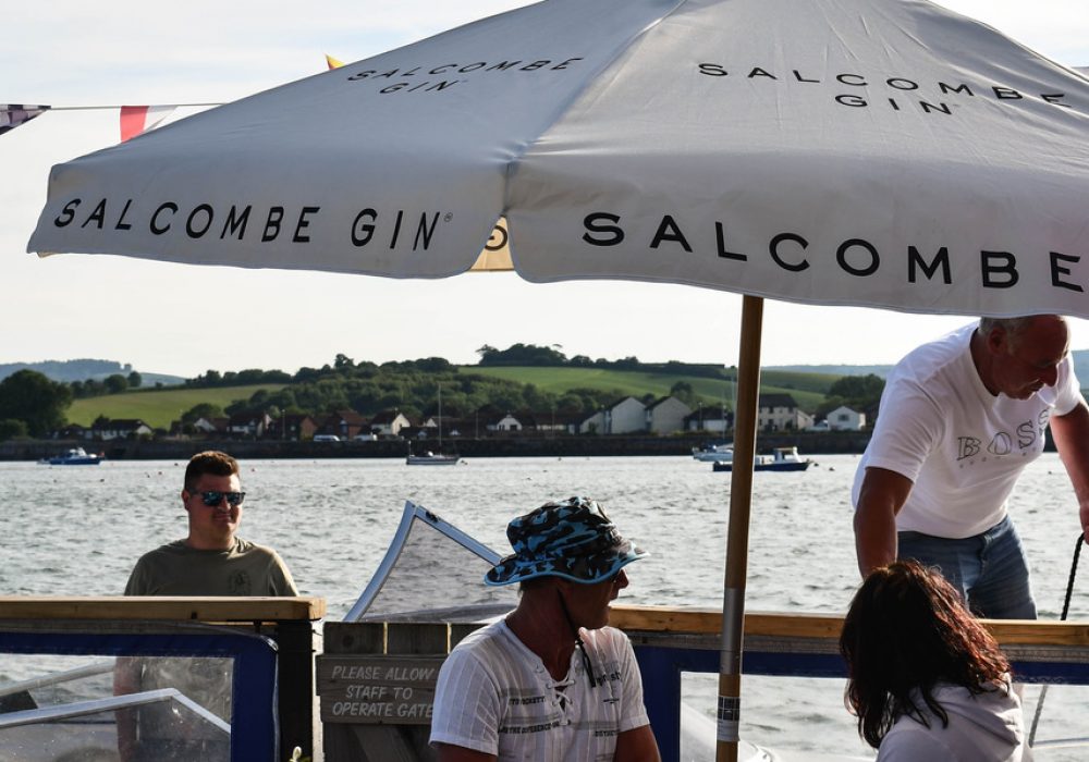 People sitting under a Salcombe Gin parasol at the River Exe Cafe