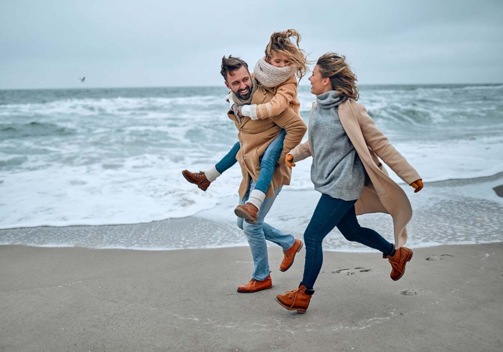 Portrait of a young married couple and their cute daughter who have fun on the beach in winter.