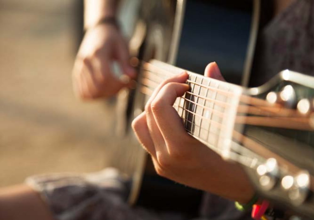 Teen girl playing acoustic guitar, detail, shallow DOF.