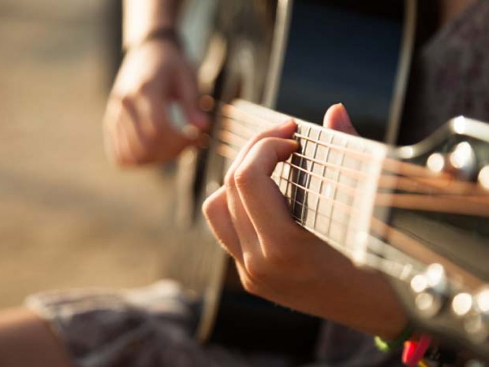 Teen girl playing acoustic guitar, detail, shallow DOF.