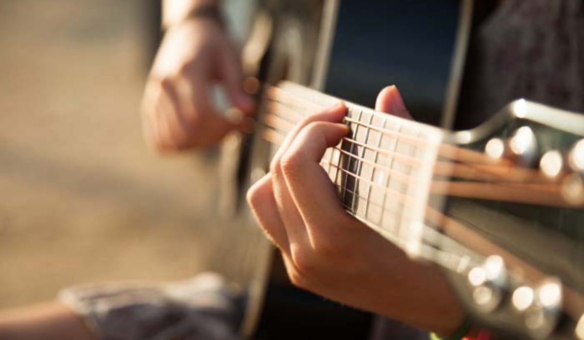 Teen girl playing acoustic guitar, detail, shallow DOF.